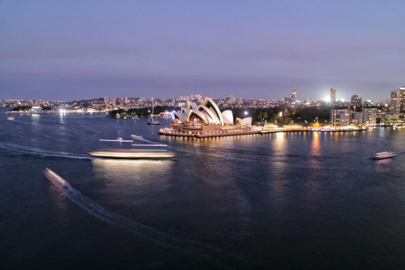 A stunning view of the Sydney Opera House and harbor illuminated at twilight, showcasing city life and architecture.