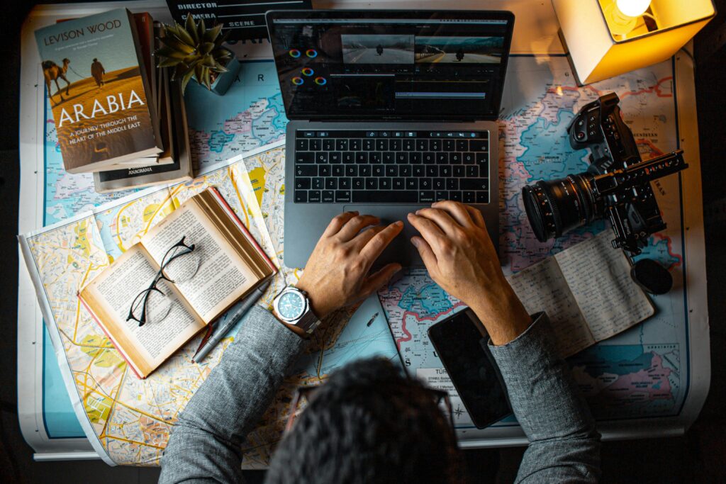 Man planning travel itinerary using laptop and maps at desk.